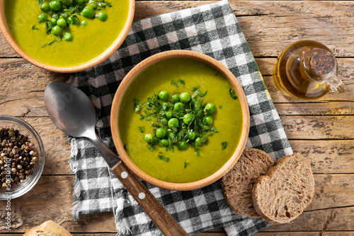 Green pea soup in a wooden bowl on rustic wooden table. Top view