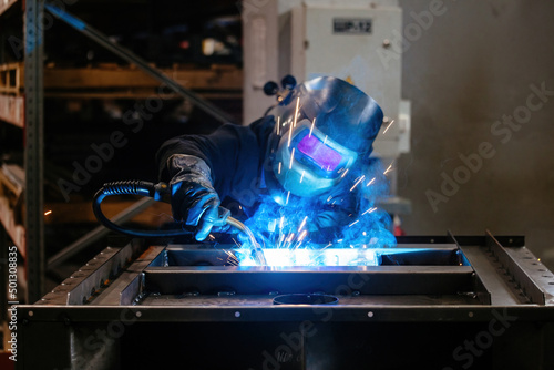 Factory worker in protective mask welding iron parts