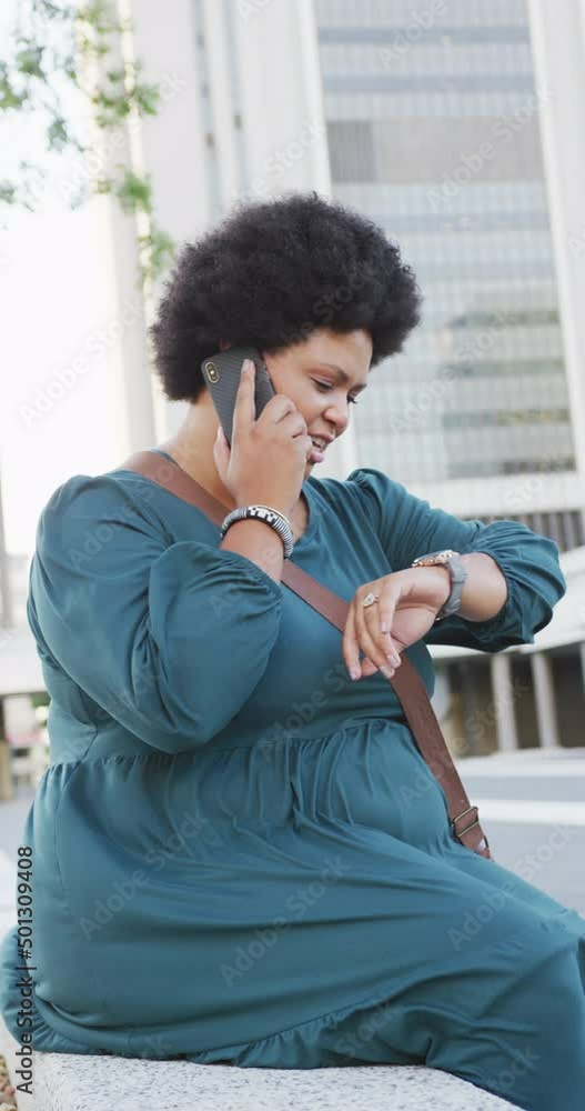 Vertical video of happy plus size biracial woman on street checking smartwatch Vertical video of happy plus size biracial woman on street checking smartwatch