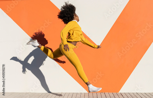 Young woman jumping by wall on footpath photo