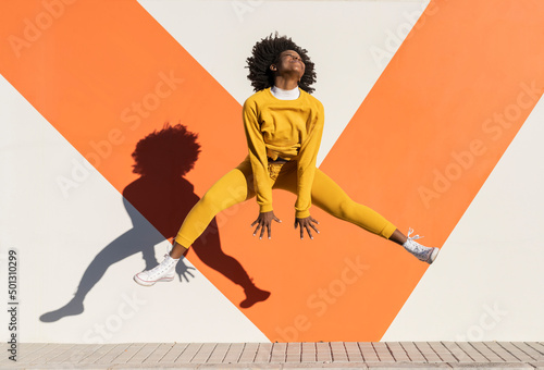 Playful young woman doing splits in air on sunny day photo