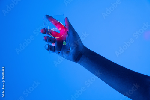 Hand of woman with stopwatch on futuristic transparent smart phone against blue background photo
