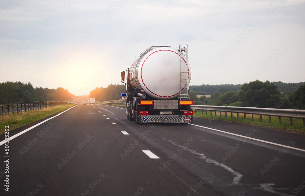 A truck with a semi-trailer transports a dangerous chemical cargo in a tank car on a highway against the background of a sunset. Sanctions in cargo transportation