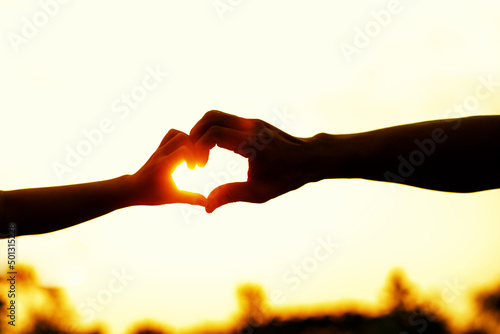 Father and child hands in shape of heart on beautiful sunset background.