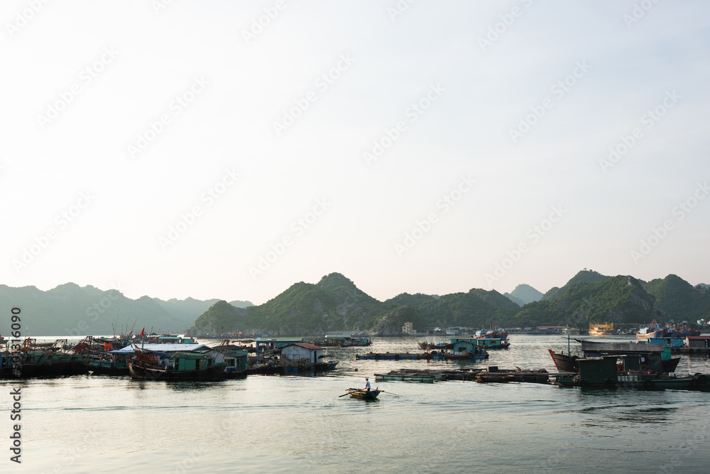Person paddles standing on his boat in the early morning by floating fishing village on Cat Ba Island, Halong Bay, Vietnam.