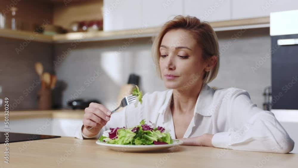 Tired woman sitting at table looking sad and bored with diet don't want to eat salad. At the kitchen. Food. Portrait. Slow motion Tired woman sitting at table looking sad and bored with diet don't want to eat salad. At the kitchen. Food. Portrait. Slow motion