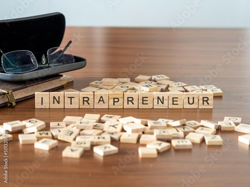 intrapreneur word or concept represented by wooden letter tiles on a wooden table with glasses and a book photo