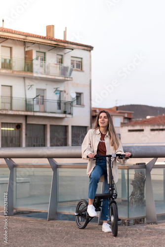 Ecologic transport for the city. Smiling young woman riding an electric bicycle with the city building behind