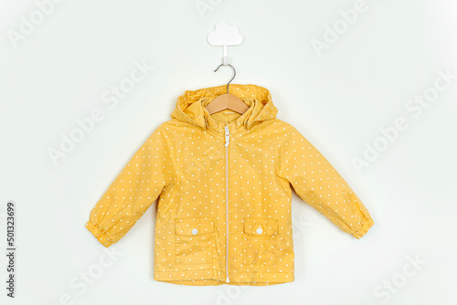 Yellow raincoat hanging on a hanger. Stylish childrens outerwear on white background. Autumn kids outfit photo