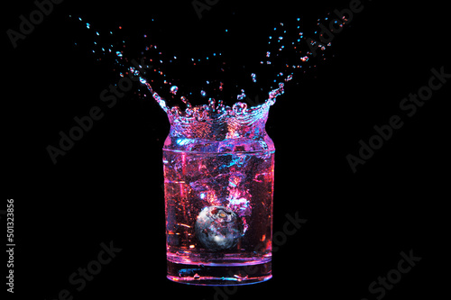 Blueberry falling into glass with colorful splashing on black background
