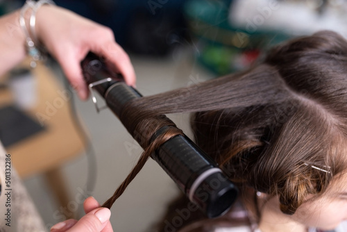 The stylist curls the girl's hair with a curling iron