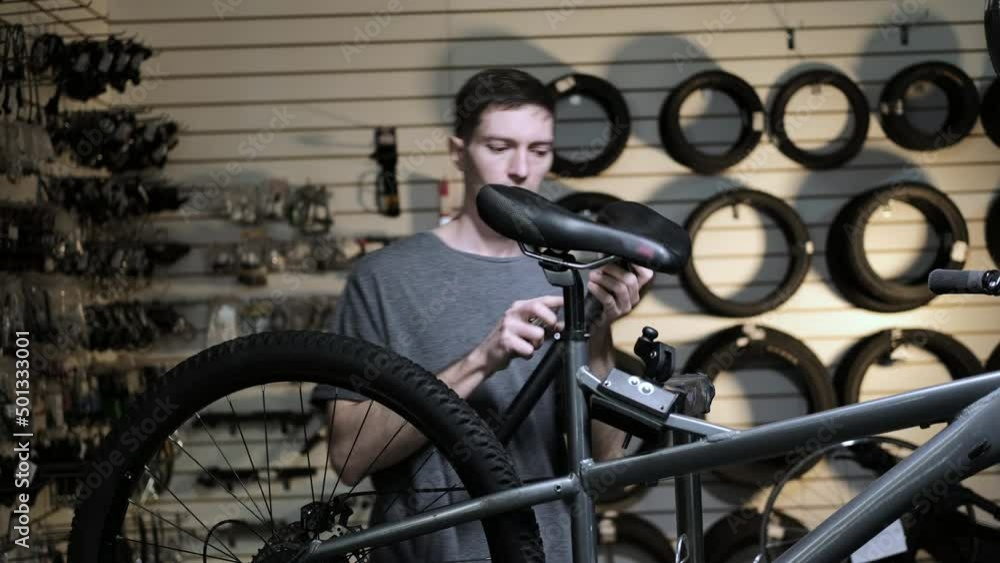Service engineer performs diagnostics and repairs of bicycle in professional workshop. Repair service for sports and mountain bikes. Mechanic tries on new bicycle seat in sports store Service engineer performs diagnostics and repairs of bicycle in professional workshop. Repair service for sports and mountain bikes. Mechanic tries on new bicycle seat in sports store