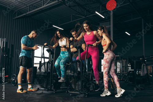 Group of young friends doing sports, training at gym indoors. Woman training at exercise bike