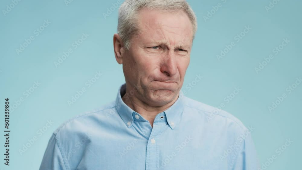 Disgust feeling. Emotional grey haired senior man feeling unpleasant smell, frowning face and gagging, blue background Disgust feeling. Emotional grey haired senior man feeling unpleasant smell, frowning face and gagging, blue background