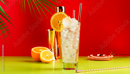 Tom Collins popular alcoholic cocktail with dry gin, syrup, lemon juice, soda, orange and ice. Bright red green summer banner background, negative space