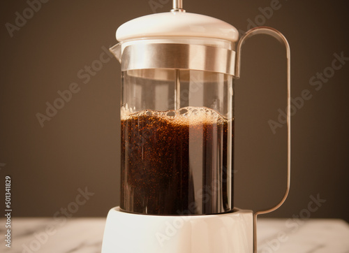 Fresh coffee in a coffee press alongside biscuits and a cup of coffee. photo