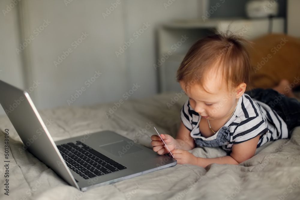 Toddler baby with laptop and bank card, online shopping and kids, toddler with laptop on bed in bedroom Toddler baby with laptop and bank card, online shopping and kids, toddler with laptop on bed in bedroom