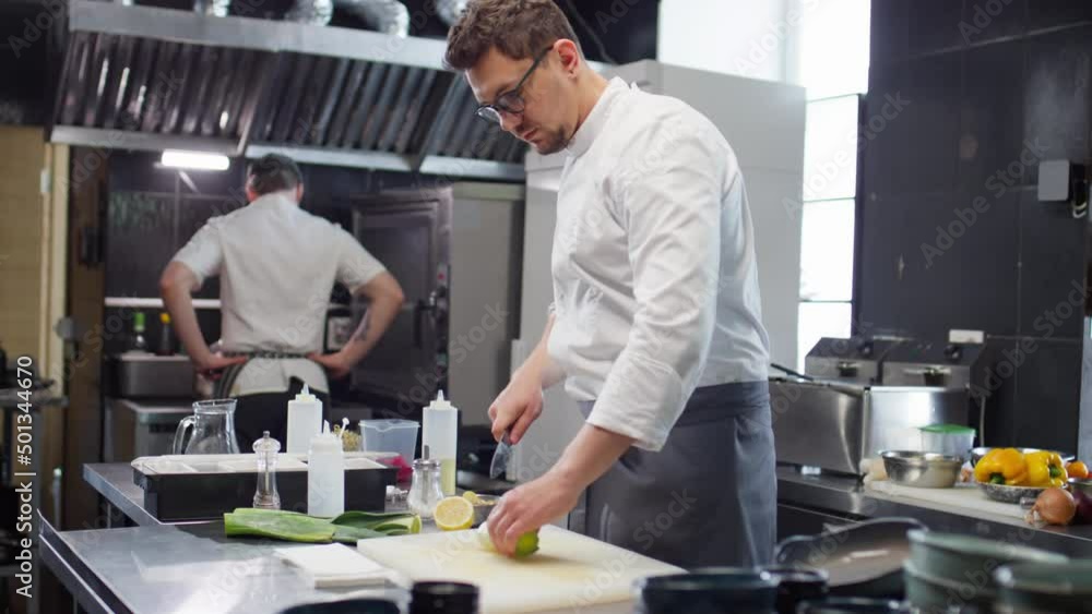 Male chef in uniform cutting fresh leeks while cooking food order in restaurant kitchen Male chef in uniform cutting fresh leeks while cooking food order in restaurant kitchen