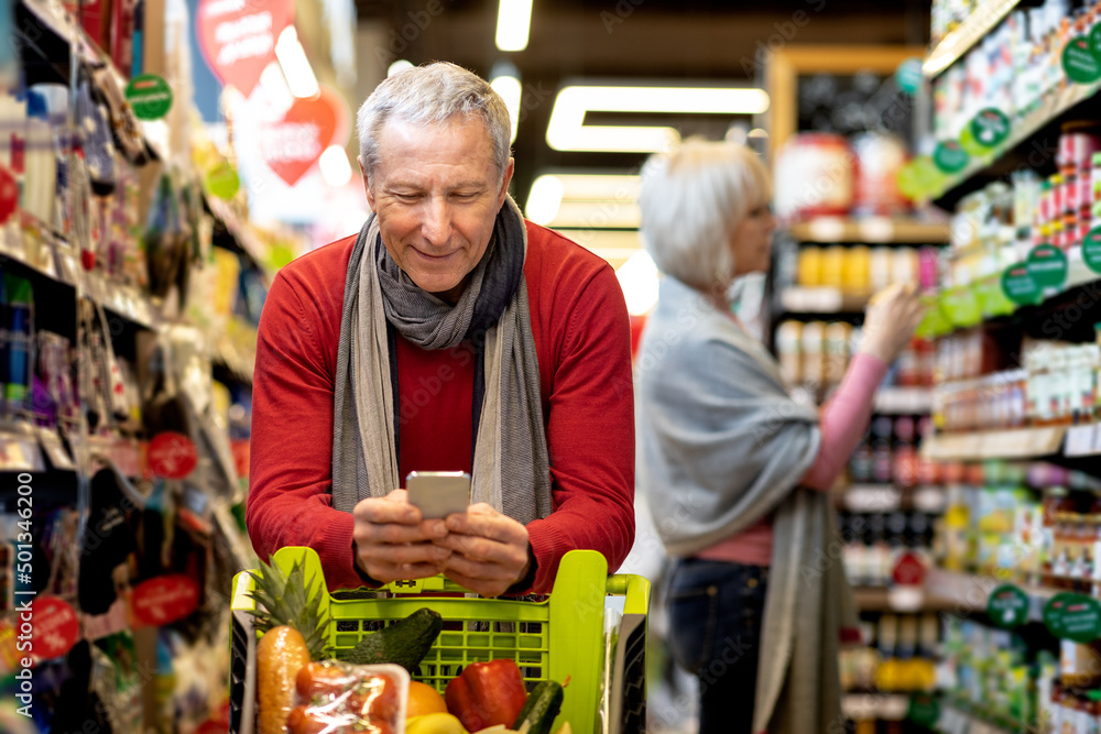 Senior man checking shopping list on smartphone, purchasing with wife