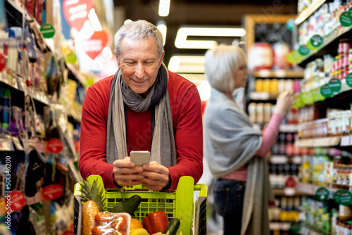 Senior man checking shopping list on smartphone, purchasing with wife