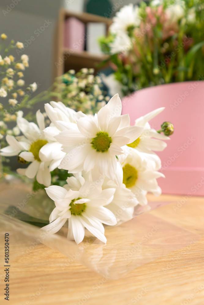 Close-up of beautiful white daisies on the table, in the background a florist makes a flower arrangement in a pink box. Vertical photo Close-up of beautiful white daisies on the table, in the background a florist makes a flower arrangement in a pink box. Vertical photo