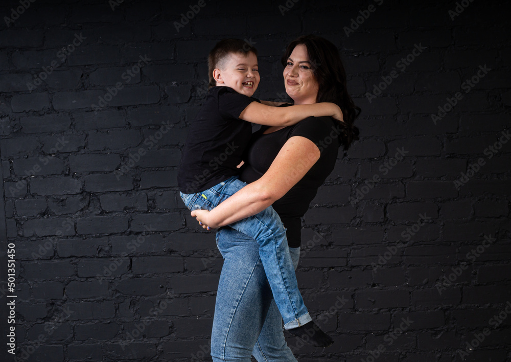 A mother in a black dress holds her son in her arms and sits on a high chair.