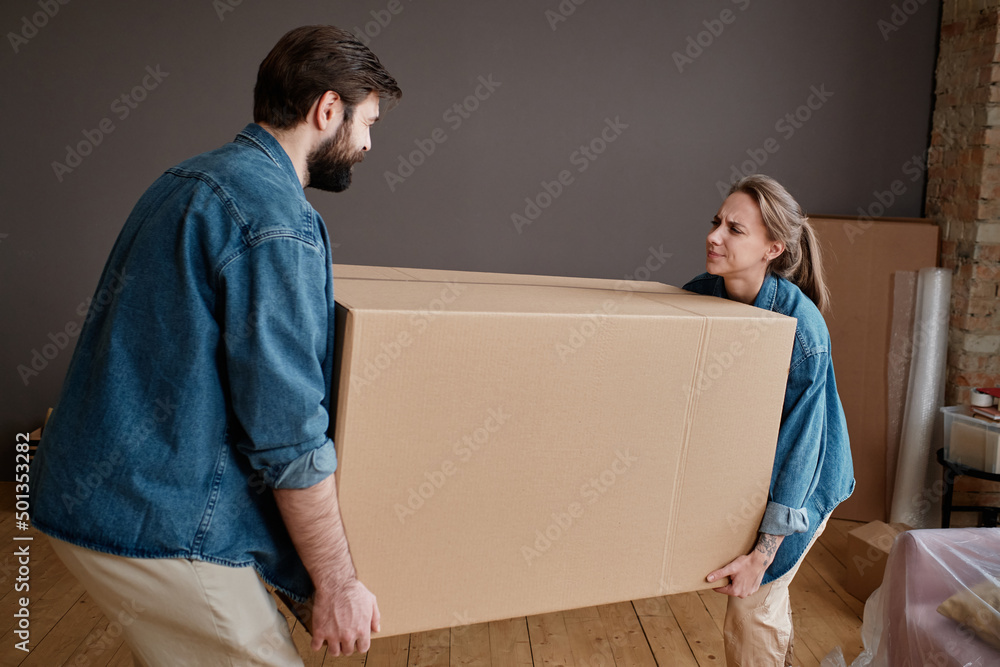 Horizontal shot of young man and woman moving to new apartment carrying big heavy box together Horizontal shot of young man and woman moving to new apartment carrying big heavy box together