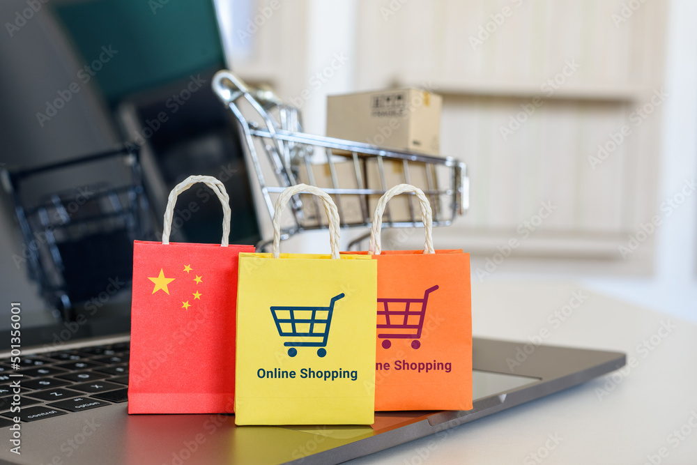 Online shopping, home shopping or product ordering, ecommerce concept : Flag of China, shopping bag with a shopping cart on a laptop keyboard, depicting buyer buys goods or services via the internet.