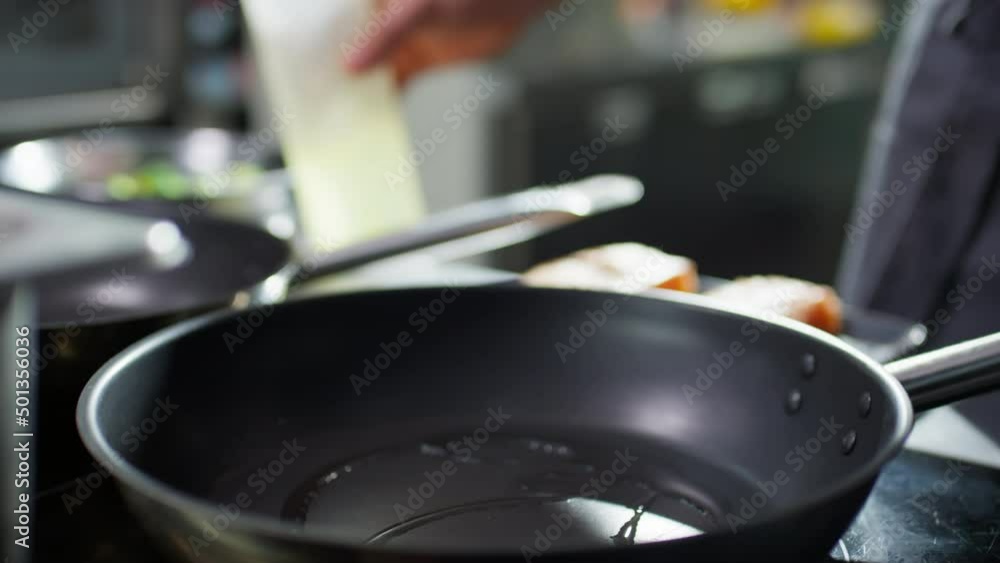 Close up shot of male chef putting salmon fillet on hot frying pan with tongues Close up shot of male chef putting salmon fillet on hot frying pan with tongues
