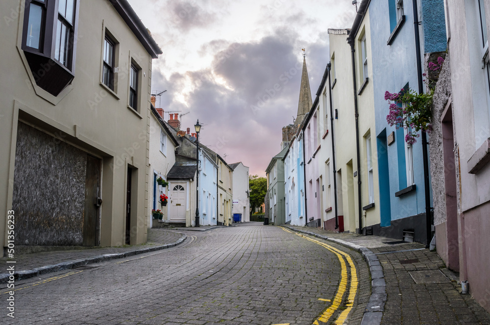 Empty cobbled street lined with pastel terraced houses at dusk. Tenby, Wales, UK.