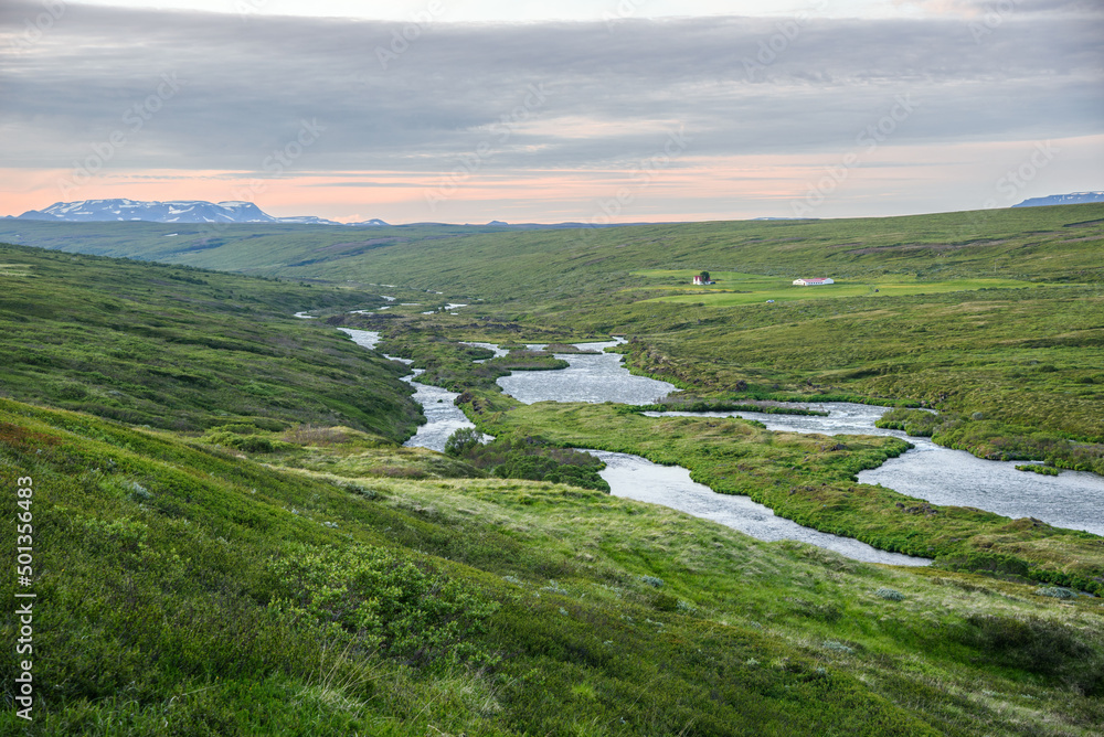 Obraz premium River at the bottom of a large green valley overlooked by a isolated farm in Iceland in summer