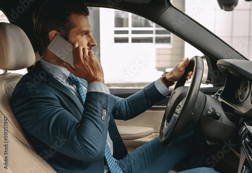 Adorable elegant businessman driving a car while having conversation on smartphone