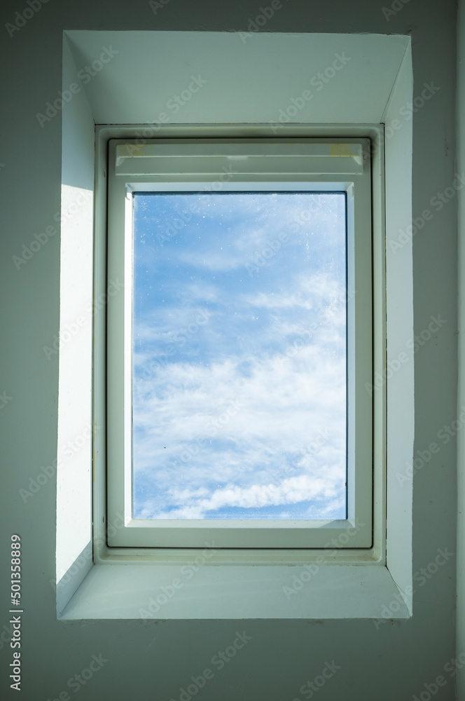 Closed roof window through which you can see the blue sky and white clouds on a sunny day. Bottom view. Closed roof window through which you can see the blue sky and white clouds on a sunny day. Bottom view.