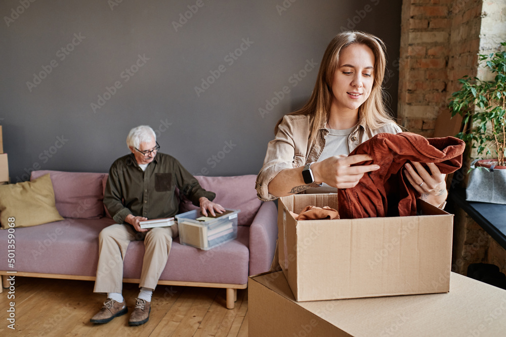 Portrait of young woman helping her grandfather to unpack clothes and stuff after moving to another apartment - obrazy, fototapety, plakaty 