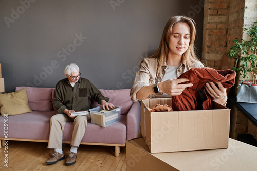 Portrait of young woman helping her grandfather to unpack clothes and stuff after moving to another apartment