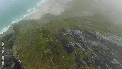 Cliffdiving at a beach (Kvalvika beach, Norway) overlooking the beach and the ocean starting at the peak of a mountain shrouded in clouds. photo