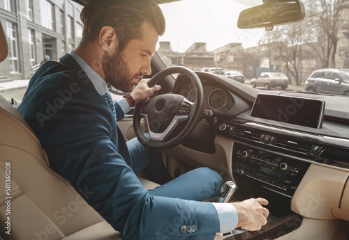 Focused handsome male in suit looking to the dashboard of automobile