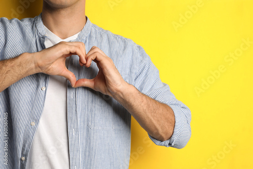 Man making heart with hands on yellow background, closeup. Space for text