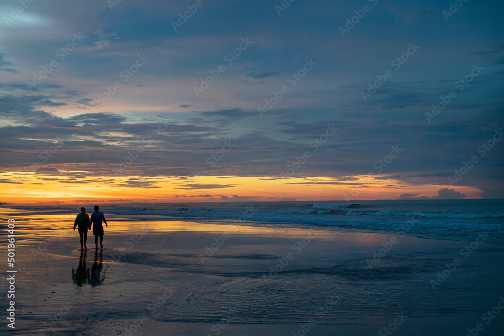 Couple walks on the beach at sunrise