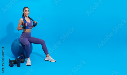 Asian beautiful happy woman holding towel and sitting on fit ball after exercise isolated on blue background. Woman healthy and exercising concept.
