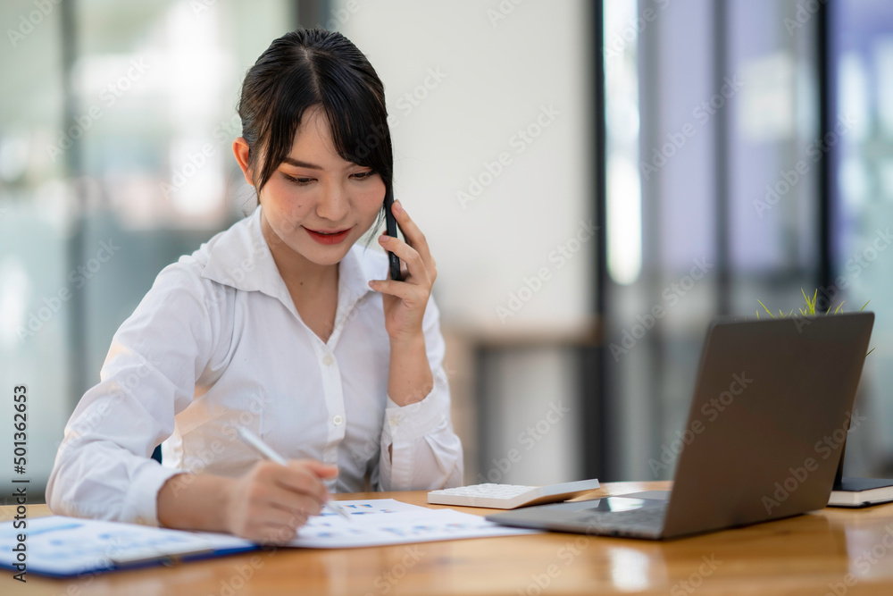 business woman using, touching on mobile smart phone screen while working on laptop computer on desk at home office, E-business, internet technology concept business woman using, touching on mobile smart phone screen while working on laptop computer on desk at home office, E-business, internet technology concept
