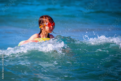 Happy child girl swimming on the waves of sea. Summer vacation and healthy lifestyle concept. Copy space.