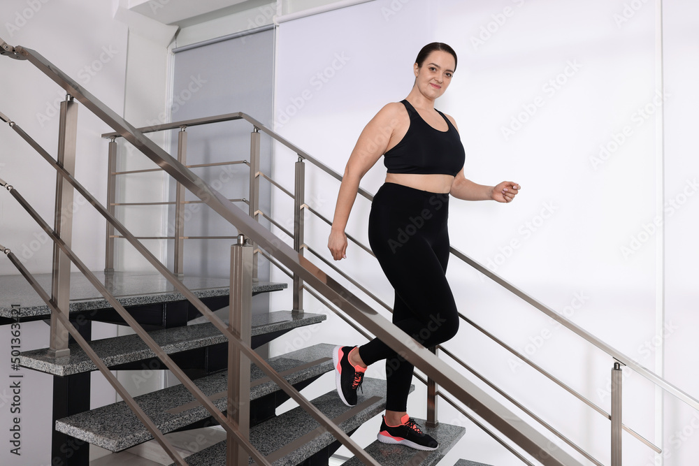 Overweight woman in sportswear running downstairs indoors Overweight woman in sportswear running downstairs indoors