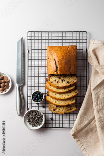 Top view vanilla cake with chocolate chip on a culinary lattice, with bowl of milk and dark chocolate drops and blueberry on a light gray background