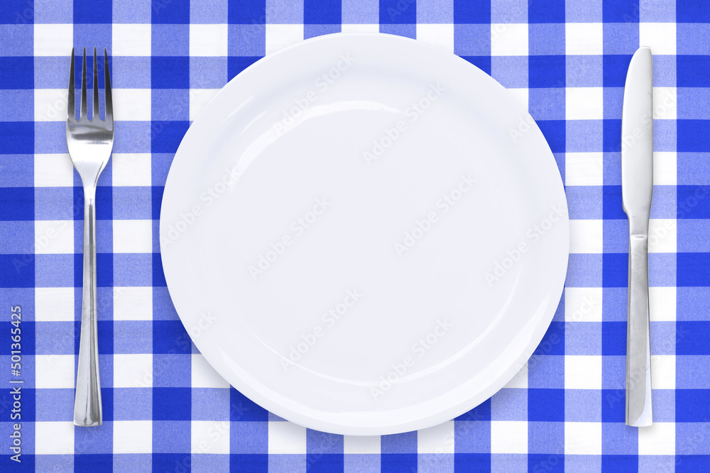 Classic cooking template - top view of an empty white ceramic plate and cutlery on a blue checked tablecloth Classic cooking template - top view of an empty white ceramic plate and cutlery on a blue checked tablecloth
