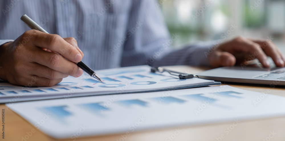 Businessman analyzing graphs working at office with laptop, tablet, and graph data documents on his desk. Businessman analyzing graphs working at office with laptop, tablet, and graph data documents on his desk.