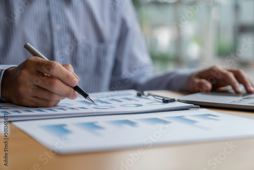 Businessman analyzing graphs working at office with laptop, tablet, and graph data documents on his desk.