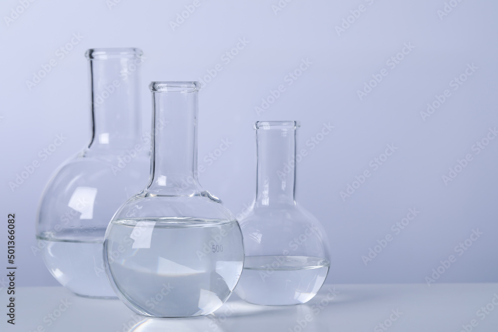Florence flasks with transparent liquid on table against light background. Space for text Florence flasks with transparent liquid on table against light background. Space for text