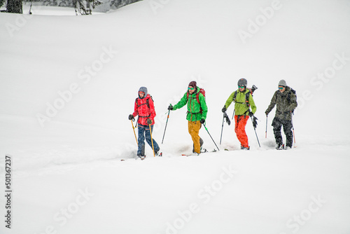 Group of male skier tourists with backpacks hiking on skis in deep snow on cold winter day