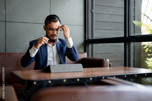 businessman looking at his laptop and is using tissue paper to wipe sweat.
